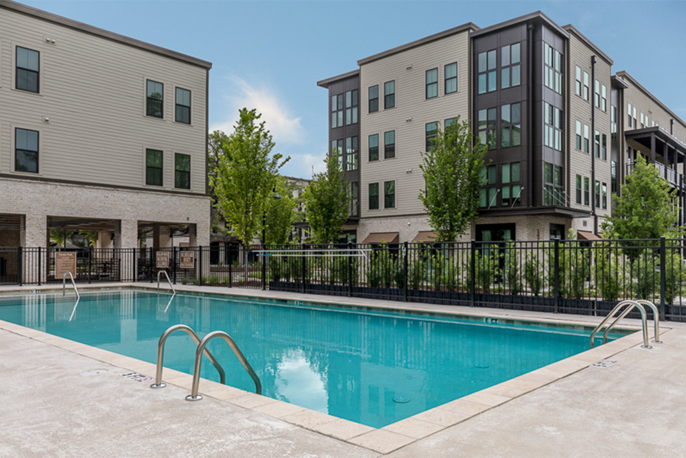 Outdoor swimming pool with metal ladders, surrounded by a concrete deck and black metal fence, set amid modern apartment buildings—an inviting amenity thoughtfully designed by multifamily general contractors dedicated to quality land development.