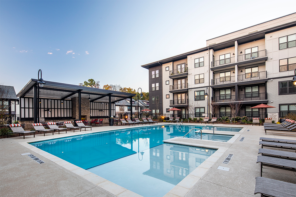 Modern apartment complex with a large outdoor swimming pool, surrounded by lounge chairs and umbrellas, showcases quality multifamily construction by leading multifamily general contractors, adjacent to a covered seating area.