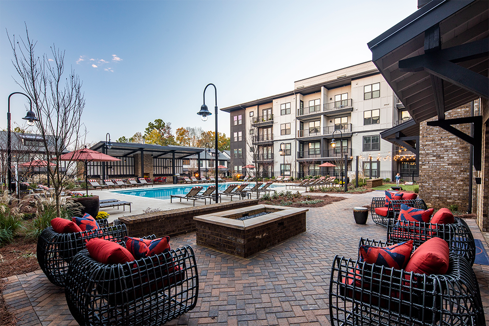 Modern apartment complex courtyard showcases market rate developments with a swimming pool, lounge chairs, fire pit, outdoor seating, and landscaped areas surrounded by multi-story buildings.