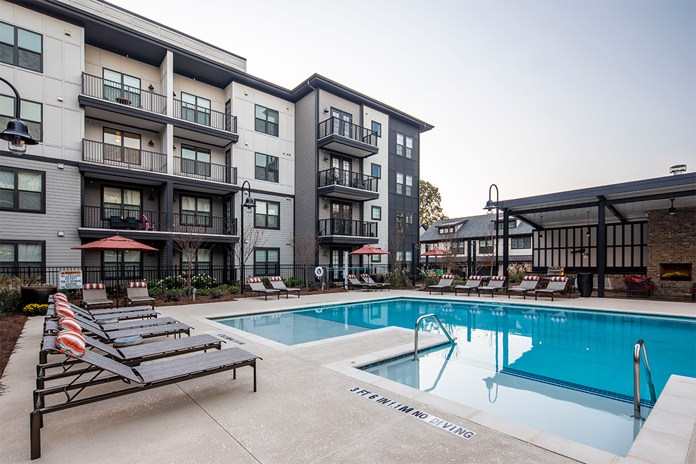 Outdoor swimming pool with lounge chairs, umbrellas, and a modern four-story apartment building in the background, showcasing exceptional multifamily construction by experienced general contractors.