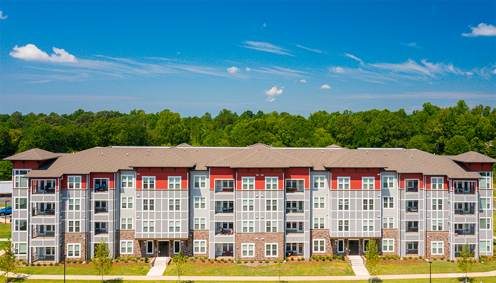 A modern four-story apartment building with balconies, set against a backdrop of trees and a clear blue sky—expertly crafted by multifamily general contractors specializing in land development.