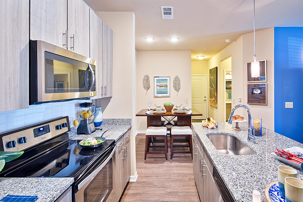 Modern kitchen with stainless steel appliances, granite countertops, and a dining table set for four in a bright, open-plan apartment—ideal for market rate developments by leading multifamily general contractors.