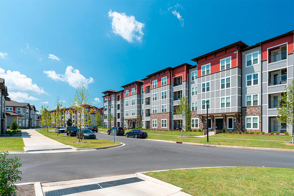 Modern apartment buildings with balconies and large windows showcase stylish multifamily construction, with cars parked along the street and landscaped grassy areas under a clear blue sky.