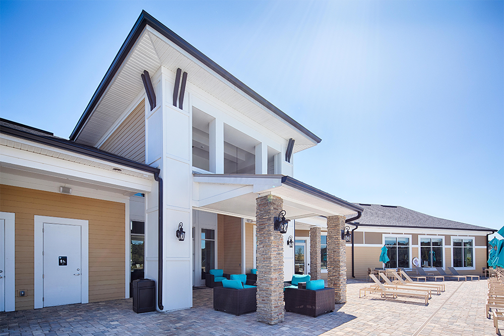 A modern clubhouse—perfect for market rate developments—with outdoor seating, stone pillars, lounge chairs, and umbrellas on a sunny day.