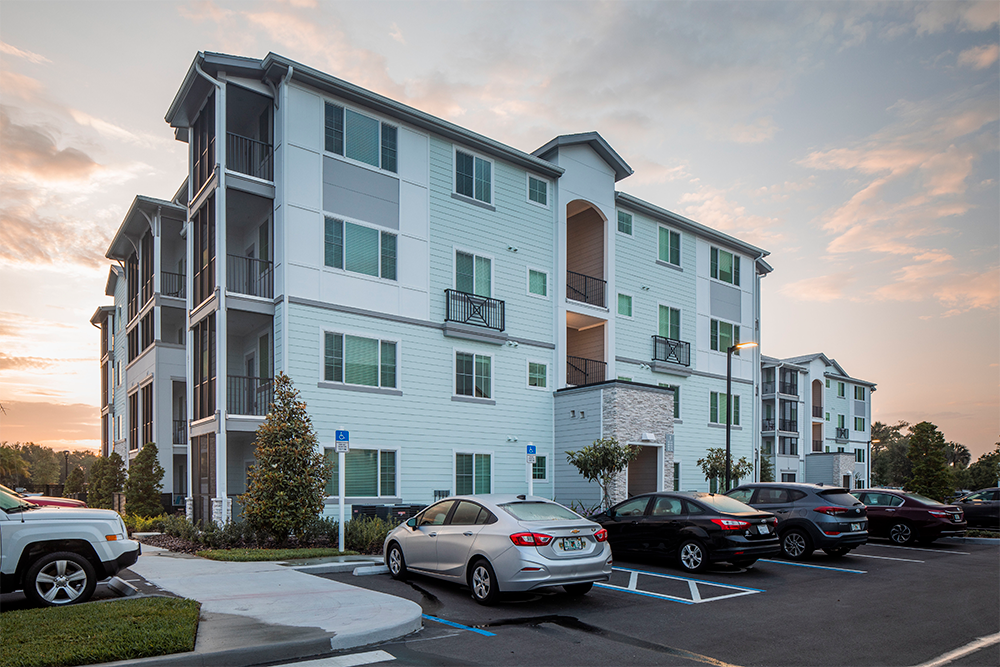 Four-story modern apartment building with balconies and parked cars in the foreground, photographed at sunset—a prime example of multifamily construction and thoughtful land development.