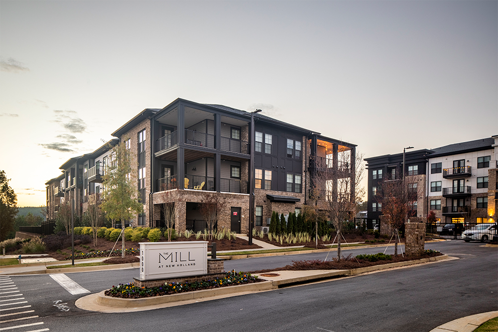 Modern three-story apartment building with balconies, stone accents, and landscaped grounds; a sign in front reads "Mill at New Holland," showcasing quality multifamily construction in desirable market rate developments.