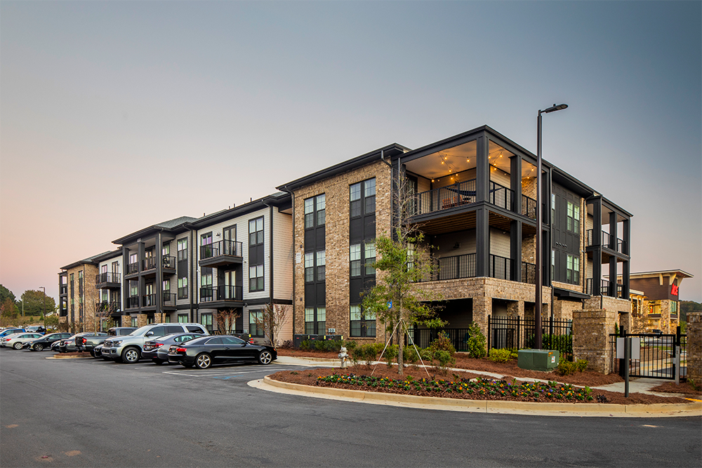 Three-story modern apartment building with balconies, brick and siding exterior, landscaped grounds, and parked cars in front at dusk—an ideal example of quality multifamily construction for market rate developments.