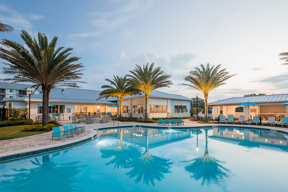 Resort-style outdoor pool with curved edges, surrounded by palm trees, lounge chairs, and two modern buildings at sunset—expertly crafted by multifamily general contractors specializing in market rate developments.