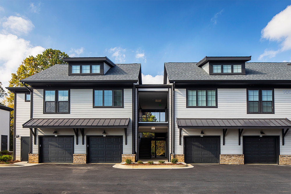 Two-story modern townhouse building with three black garage doors, gray siding, brick accents, and an open central staircase under a blue sky—an ideal example of market rate developments by expert multifamily general contractors.