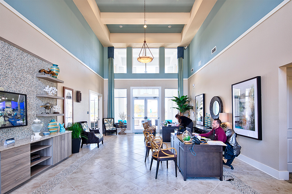 Spacious, modern office lobby with high ceiling, large windows, two people working at desks—an inviting space often seen in market rate developments by experienced multifamily general contractors. Seating area with decor on the left.