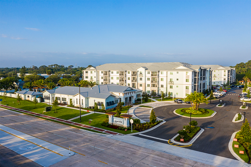 Aerial view of a modern apartment complex with white buildings, manicured lawns, a circular driveway, and a main road in the foreground—an example of market rate developments shaped by leading multifamily general contractors.