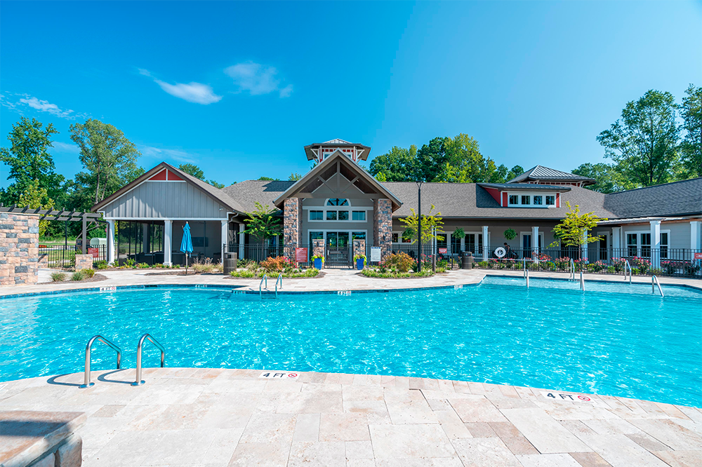 Outdoor swimming pool in front of a modern clubhouse building, featuring lounge chairs, trees, and clear blue sky—an inviting amenity often seen in market rate developments by leading multifamily general contractors.