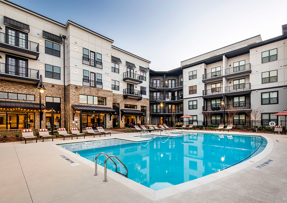 Modern apartment complex featuring multifamily construction, three stories, and balconies overlooking an outdoor swimming pool with lounge chairs and umbrellas on the pool deck.