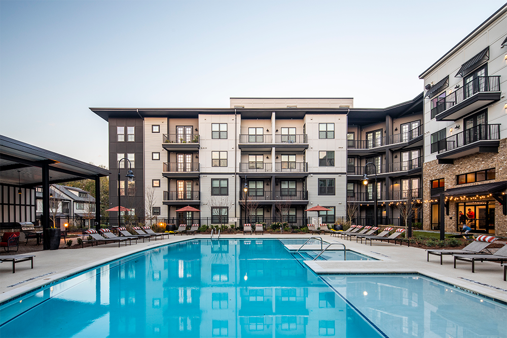 Modern apartment complex with multiple balconies, lounge chairs, and a large outdoor swimming pool, photographed in daylight with a clear sky—an ideal example of multifamily construction for market rate developments.