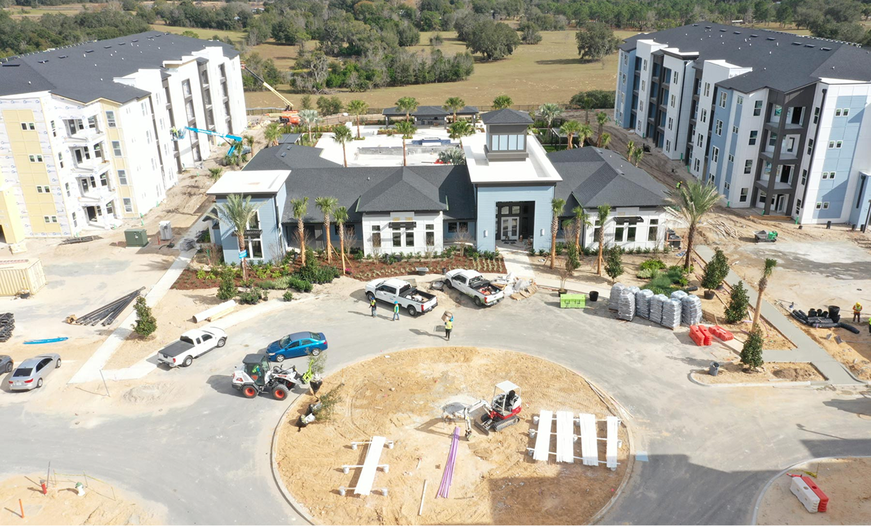 Aerial view of an apartment complex under construction with workers, vehicles, and building materials around a central roundabout—showcasing the expertise of multifamily general contractors on market rate developments.