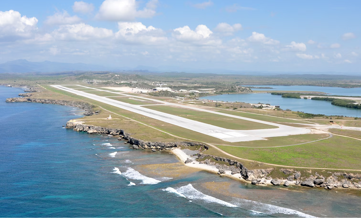 Aerial view of a coastal airport runway with adjacent buildings, bordered by the ocean on one side and inland water and greenery on the other, highlights nearby land development opportunities perfect for future multifamily construction.